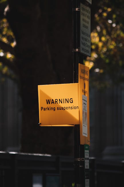 Close-up of a blue parking sign indicating designated parking for disabled individuals and vans, situated outdoors under a roof structure with visible support beams. The sign displays the wheelchair symbol at the top, followed by the text 'PARKING ONLY VAN ACCESSIBLE' and a minimum fine of '250 dollars'. The sign is mounted on a metal pole with a small blank blue panel below it. The environment suggests a loading or unloading area, possibly near a residential or commercial property on Colham Road in Yiewsley, relevant to house removals and moving services offered by Man with Van Yiewsley. The image emphasizes the importance of parking regulations for efficient furniture transport and home relocation logistics.